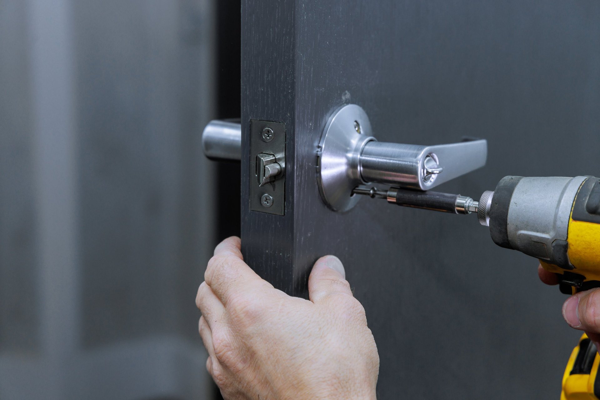 Installing lock handles on room doors with screwdriver by carpenter
