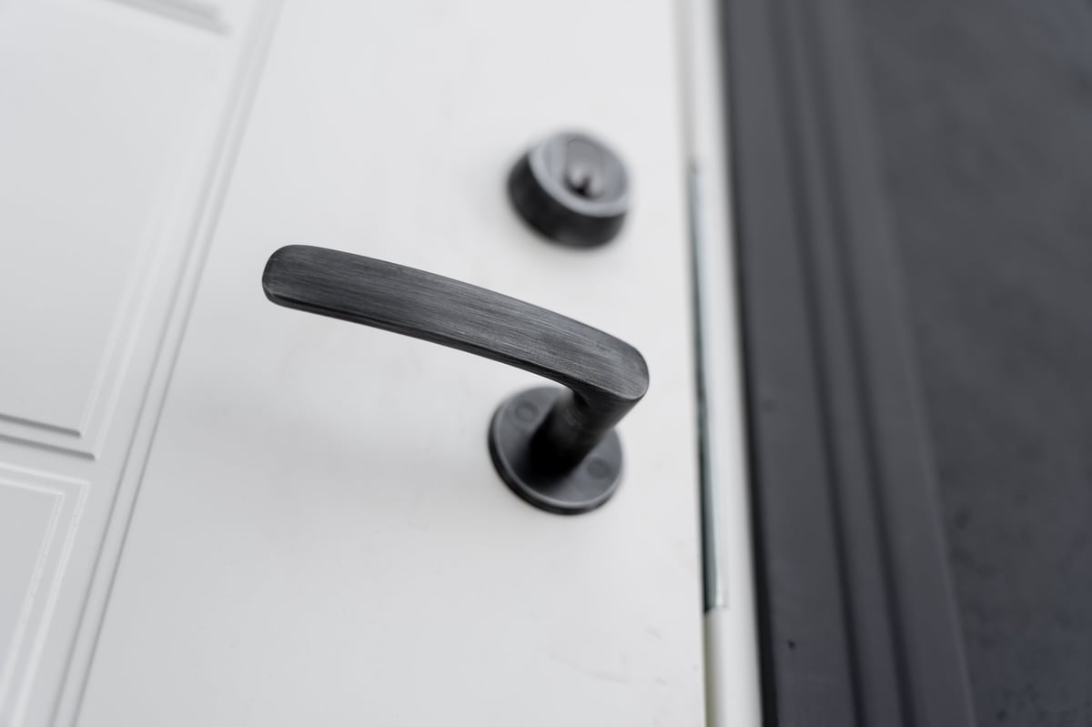Black door lever handle in close view on white residential door, soft focus background and lock above