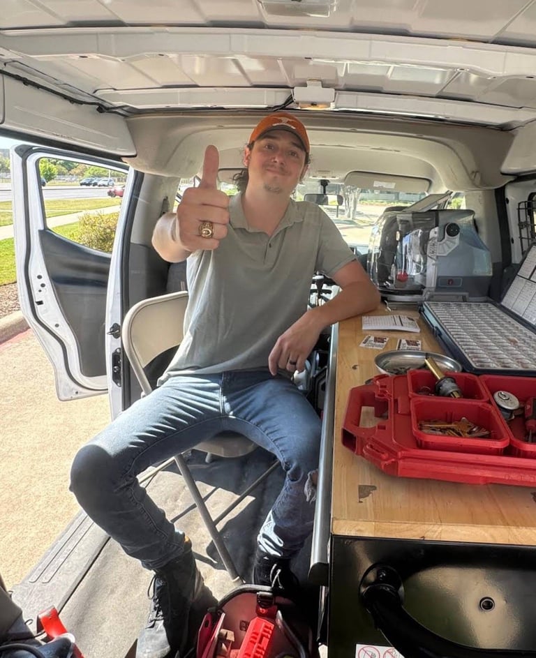 Man in work van interior holding up thumbs up, wearing cap and gray shirt, with tool organizer and red toolbox visible