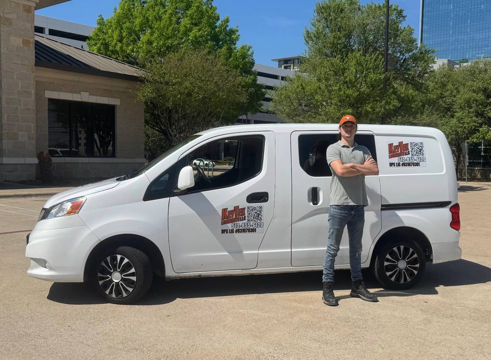 Man standing beside white service van in parking lot with trees and buildings in background