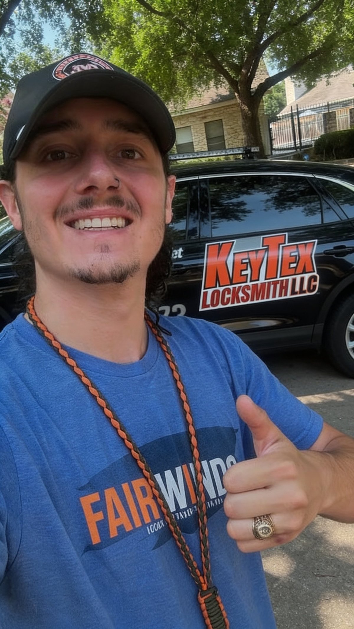 Man in blue Fairwind shirt and black cap smiling in front of KeyTex Locksmith LLC vehicle on a residential street