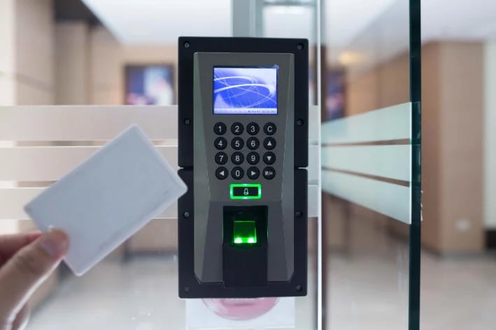 Hand holding access card near biometric door lock with fingerprint scanner and numeric keypad